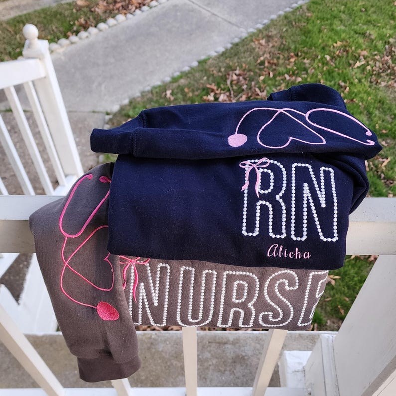 A collection of custom embroidered grey nurse shirts with various titles and names embroidered on the left side of the chest.