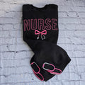 Black sweatshirt with embroidered pink text spelling 'NURSE' and a heart-shaped bow design underneath.