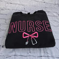 Black sweatshirt with embroidered pink text spelling 'NURSE' and a heart-shaped bow design underneath.