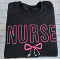 Black sweatshirt with embroidered pink text spelling 'NURSE' and a heart-shaped bow design underneath.