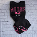 Black sweatshirt with embroidered pink text spelling 'NURSE' and a heart-shaped bow design underneath.