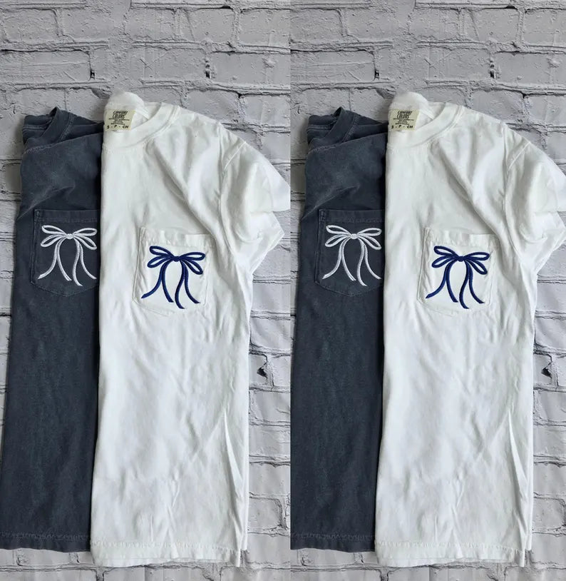 White shirt with blue embroidered bow and navy pants with white embroidered bow on a plain background