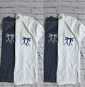 Two pairs of pants, one white and one black, with decorative bow designs on a brick wall background.