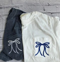 Two pieces of clothing with embroidered bows on a gray textured surface