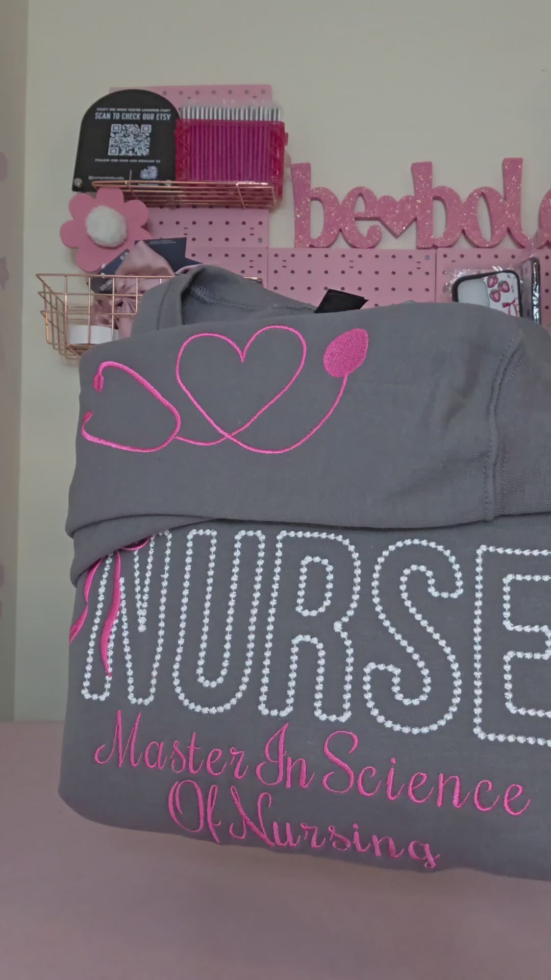 A collection of custom embroidered grey nurse shirts with various titles and names embroidered on the left side of the chest.