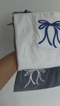 White shirt with blue embroidered bow and navy pants with white embroidered bow on a plain background